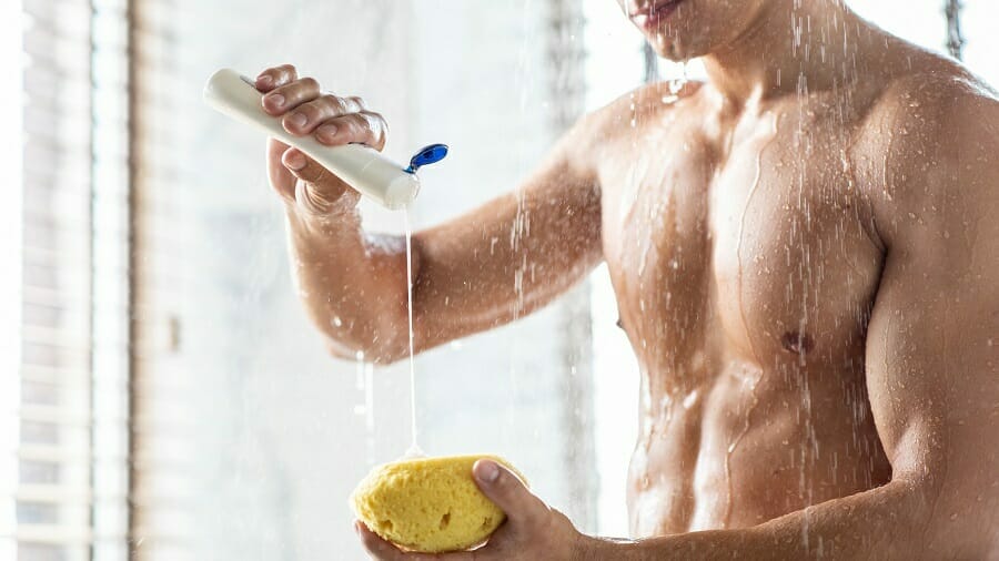 Man taking a shower pouring shampoo onto yellow sponge