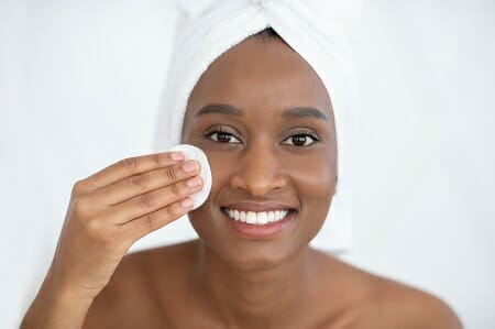 Young woman with glowing skin applying face cream with cloth